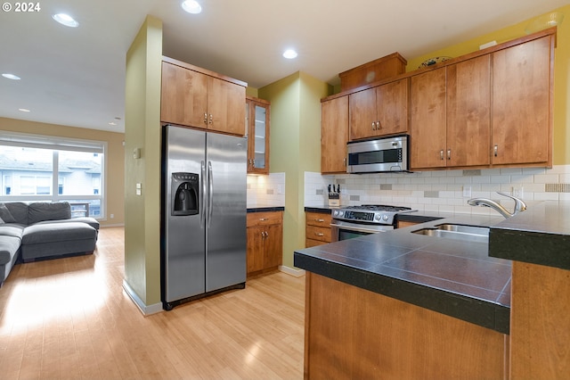 kitchen with tasteful backsplash, sink, stainless steel appliances, and light hardwood / wood-style floors