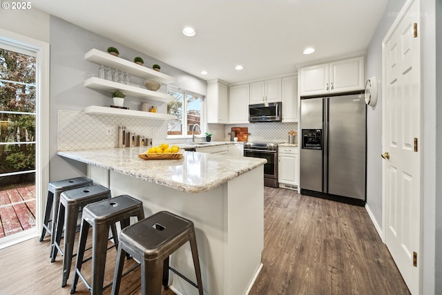 kitchen featuring white cabinetry, appliances with stainless steel finishes, a kitchen bar, and kitchen peninsula