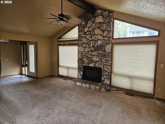 unfurnished living room featuring carpet, a stone fireplace, ceiling fan, a textured ceiling, and beamed ceiling