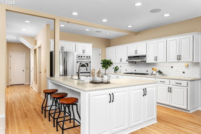 kitchen with stainless steel appliances, sink, a center island with sink, light hardwood / wood-style floors, and white cabinetry