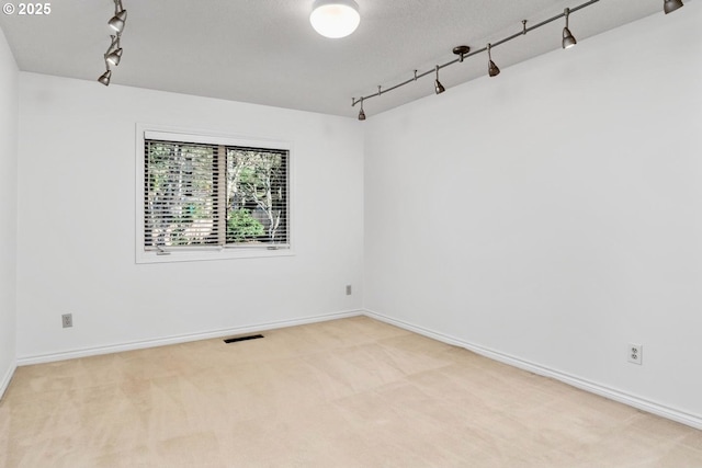 carpeted empty room with a textured ceiling and rail lighting