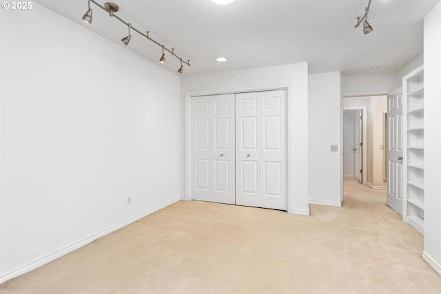 unfurnished bedroom featuring rail lighting, light colored carpet, and a closet