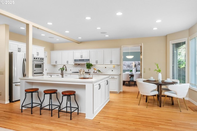 kitchen featuring a center island with sink, white cabinets, light wood-type flooring, and appliances with stainless steel finishes