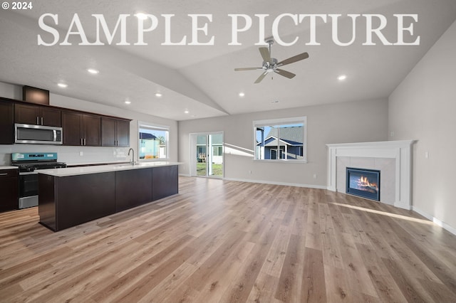 kitchen featuring light hardwood / wood-style floors, stainless steel appliances, a center island with sink, and a fireplace