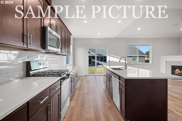 kitchen featuring appliances with stainless steel finishes, pendant lighting, a center island with sink, and light wood-type flooring