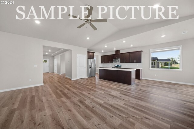 kitchen with ceiling fan, stainless steel appliances, vaulted ceiling, wood-type flooring, and an island with sink