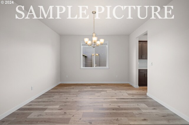 empty room featuring a notable chandelier and light wood-type flooring