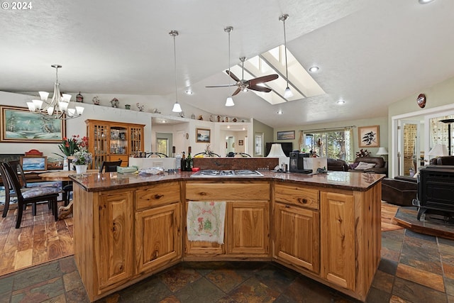 kitchen with a kitchen island with sink, vaulted ceiling with skylight, stainless steel gas cooktop, ceiling fan with notable chandelier, and dark stone counters