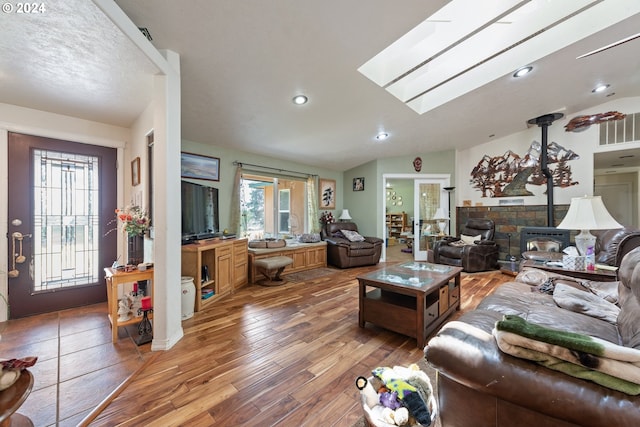 living room featuring dark wood-type flooring, vaulted ceiling with skylight, and a wood stove