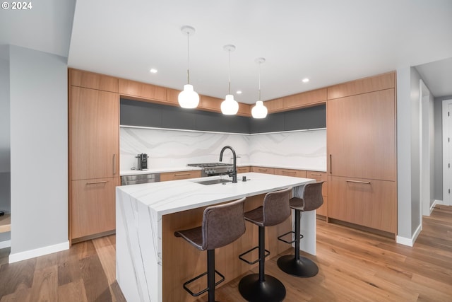 kitchen featuring pendant lighting, sink, an island with sink, tasteful backsplash, and light hardwood / wood-style floors