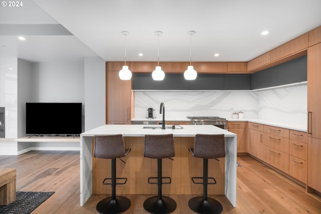 kitchen with decorative light fixtures, light hardwood / wood-style floors, a center island with sink, and sink