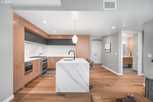 kitchen featuring a kitchen island with sink, sink, decorative light fixtures, light hardwood / wood-style floors, and stainless steel appliances