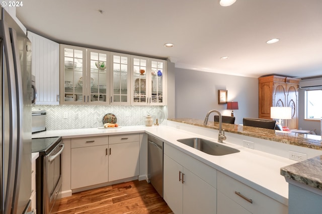 kitchen with sink, stainless steel appliances, kitchen peninsula, white cabinets, and hardwood / wood-style flooring