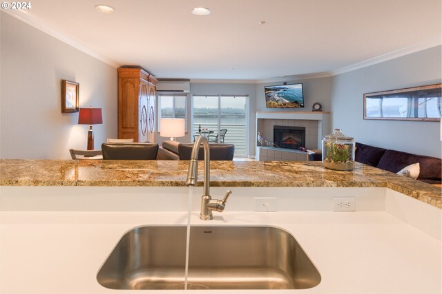 kitchen featuring sink, a wall mounted air conditioner, light stone counters, a tiled fireplace, and ornamental molding