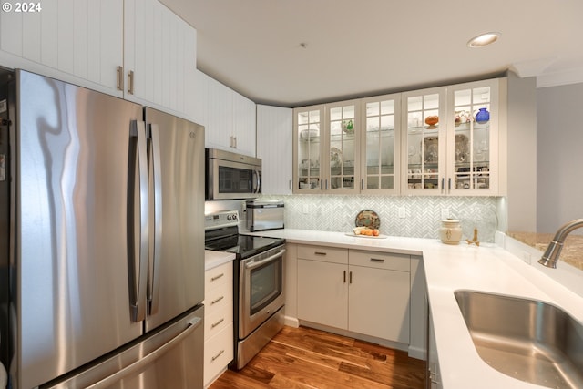 kitchen featuring decorative backsplash, appliances with stainless steel finishes, sink, hardwood / wood-style floors, and white cabinetry