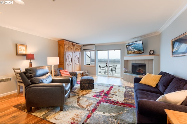 living room with a wall mounted air conditioner, a tiled fireplace, crown molding, and light hardwood / wood-style flooring