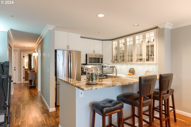 kitchen featuring stainless steel appliances, dark hardwood / wood-style floors, kitchen peninsula, a kitchen bar, and white cabinets