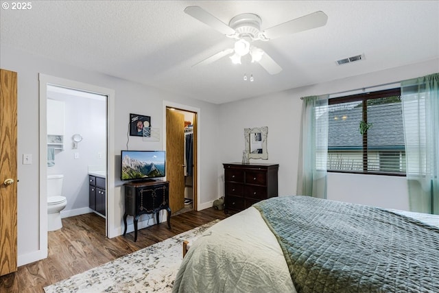 bedroom featuring a walk in closet, ensuite bath, a textured ceiling, ceiling fan, and hardwood / wood-style floors