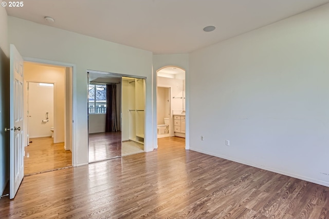 unfurnished bedroom with hardwood / wood-style floors, ensuite bath, and a closet