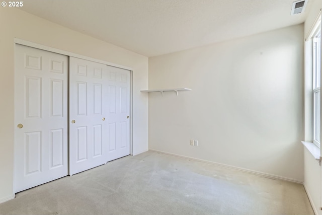 unfurnished bedroom with multiple windows, light carpet, and a closet