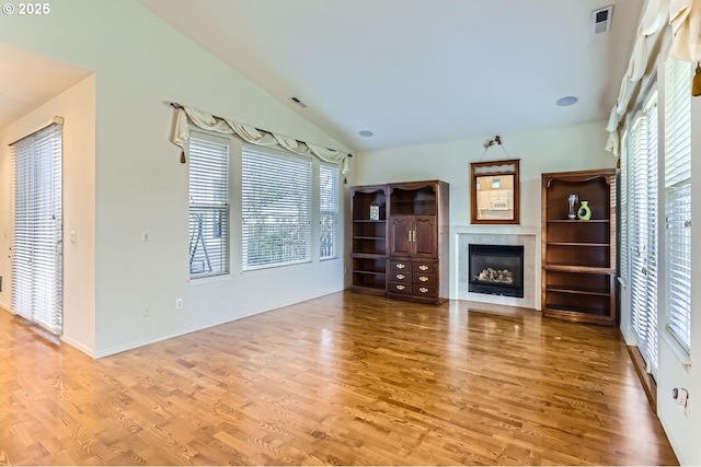 unfurnished living room with a tile fireplace, a healthy amount of sunlight, lofted ceiling, and hardwood / wood-style flooring