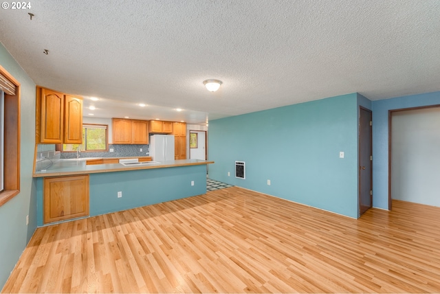 kitchen with kitchen peninsula, a textured ceiling, light hardwood / wood-style floors, and white fridge