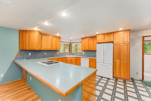 kitchen with kitchen peninsula, decorative backsplash, sink, and white appliances