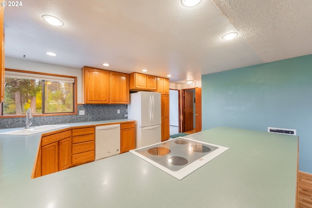 kitchen with white appliances, sink, a textured ceiling, tasteful backsplash, and light hardwood / wood-style floors