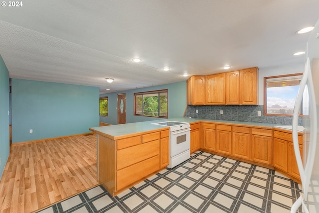 kitchen featuring white range oven, kitchen peninsula, backsplash, and a healthy amount of sunlight