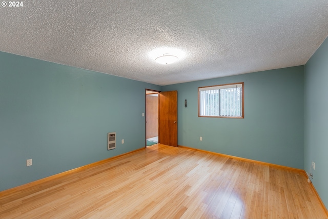 spare room featuring wood-type flooring, a textured ceiling, and heating unit