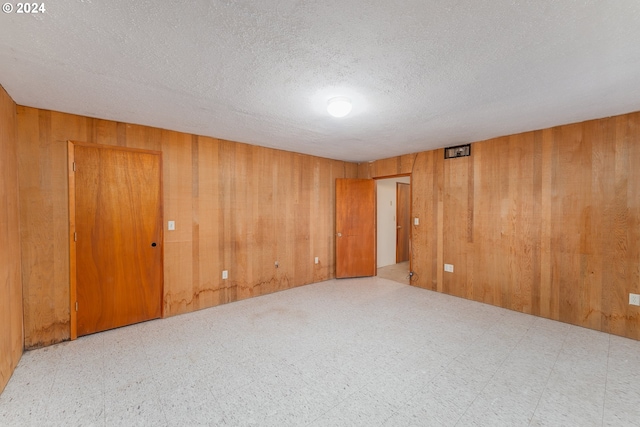 empty room featuring a textured ceiling and wooden walls