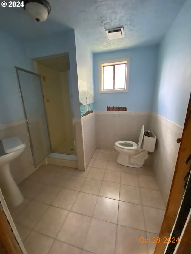 bathroom with toilet, tile walls, tile patterned floors, and walk in shower