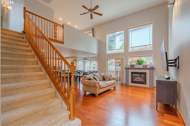 living room featuring ceiling fan, hardwood / wood-style flooring, a high ceiling, and a tile fireplace