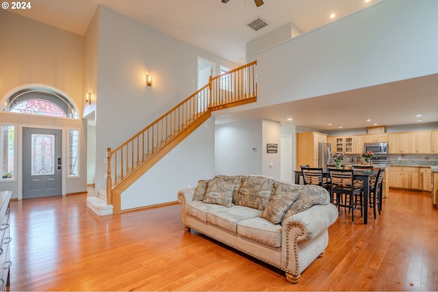 living room featuring a high ceiling, light hardwood / wood-style flooring, and ceiling fan