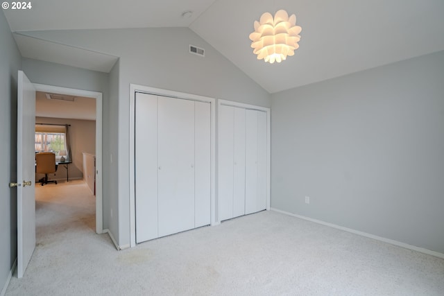 unfurnished bedroom featuring lofted ceiling, two closets, and light colored carpet