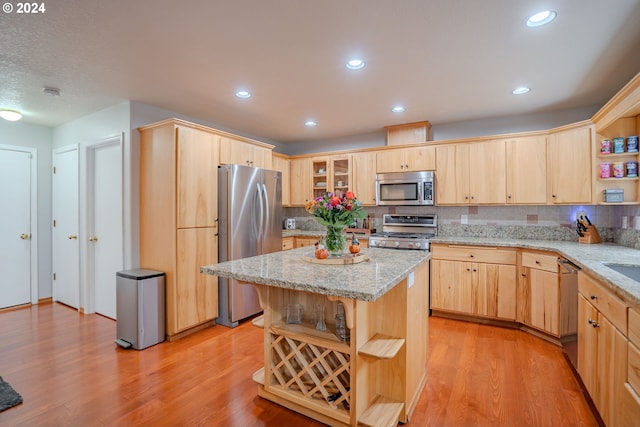 kitchen with light hardwood / wood-style floors, appliances with stainless steel finishes, light stone counters, and a kitchen island