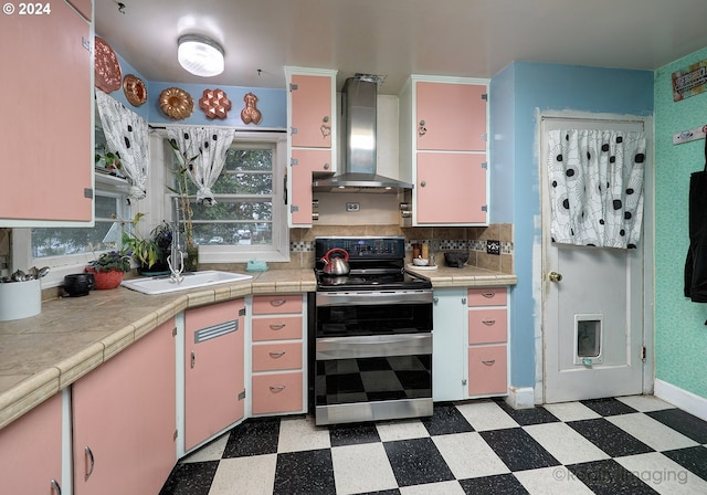 kitchen with tile counters, wall chimney exhaust hood, sink, and stainless steel range with electric cooktop