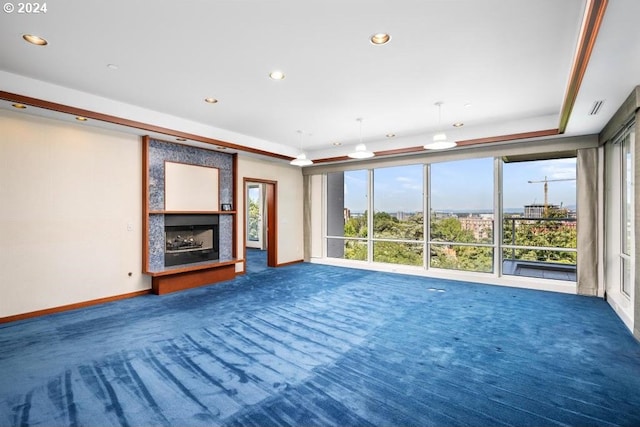 unfurnished living room with a raised ceiling, plenty of natural light, a large fireplace, and carpet flooring