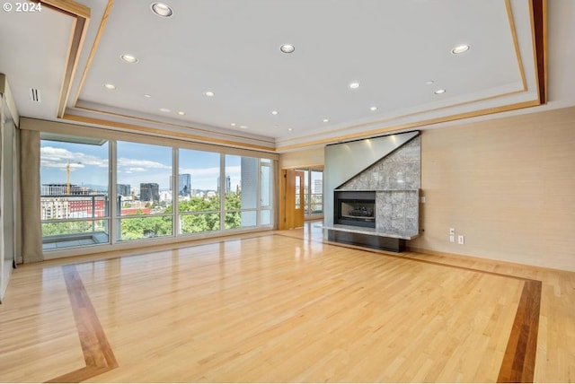 unfurnished living room with crown molding, a tray ceiling, light hardwood / wood-style floors, and a large fireplace