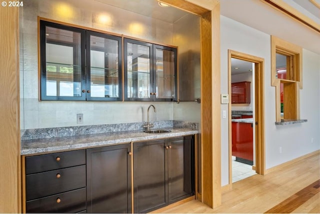 bar featuring light stone counters, sink, and light hardwood / wood-style flooring