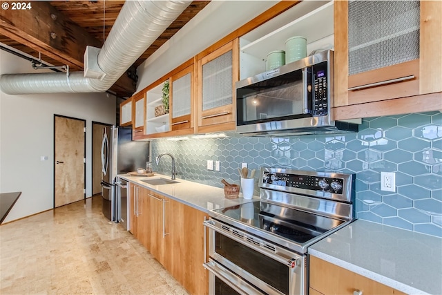 kitchen with light stone countertops, appliances with stainless steel finishes, tasteful backsplash, and sink