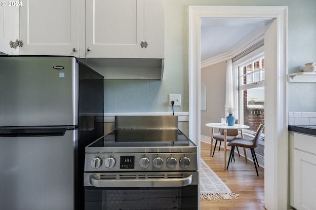 kitchen featuring white cabinets, hardwood / wood-style floors, range hood, crown molding, and stainless steel appliances