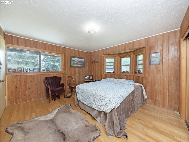 bedroom featuring wooden walls, light hardwood / wood-style flooring, and a textured ceiling