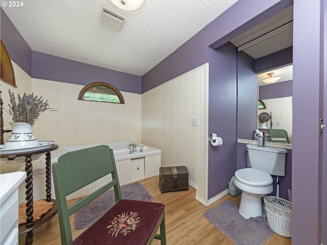 bathroom featuring hardwood / wood-style flooring, toilet, a bath, and a textured ceiling