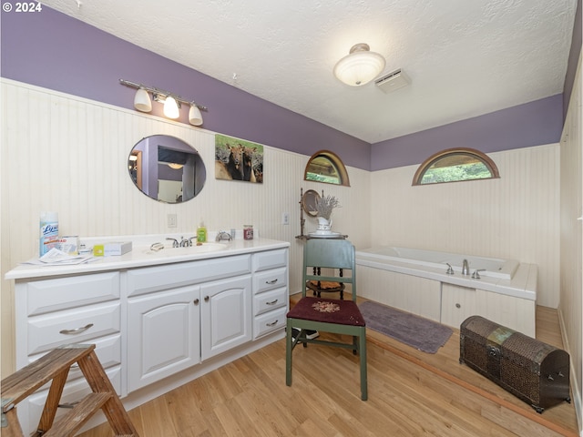 bathroom with a tub, vanity, wood-type flooring, and a textured ceiling