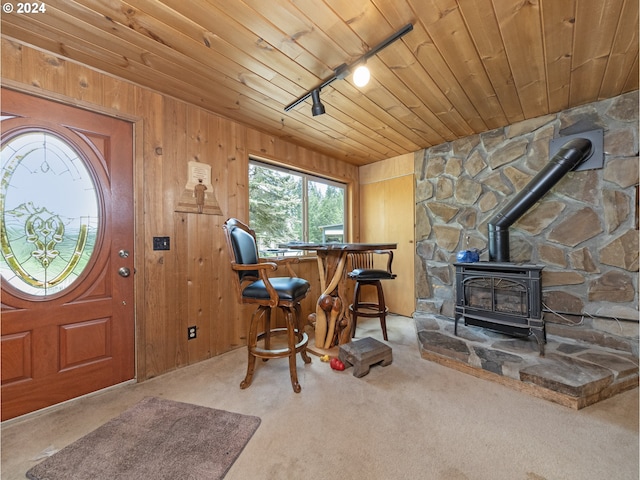 carpeted entryway featuring track lighting, wooden ceiling, bar area, a wood stove, and wood walls