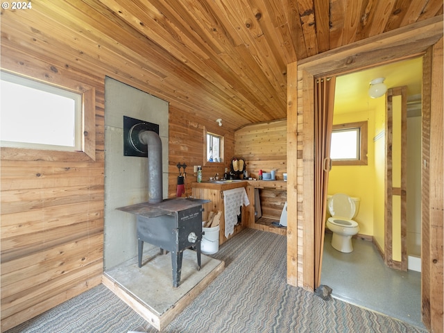 interior space featuring a wood stove, wood walls, wooden ceiling, and vaulted ceiling