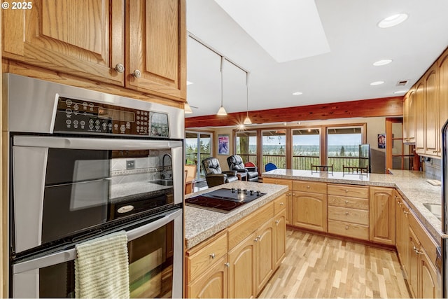 kitchen featuring a skylight, black electric stovetop, light wood-type flooring, double oven, and light brown cabinetry