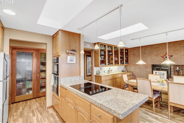 kitchen featuring light wood-type flooring, a skylight, brick wall, pendant lighting, and appliances with stainless steel finishes