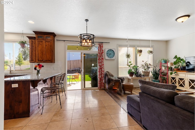 tiled living room featuring sink, a chandelier, a textured ceiling, and a healthy amount of sunlight